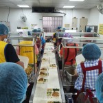 新業(yè)同仁與志工們繫上圍裙、套上防塵帽，戴上口罩，手捧一份份飯包各司其職，為的是準時將熱騰騰的飯包送到長輩手中。