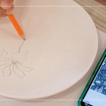 筆尖在素色瓷胚上，輕輕滑過，對照著手機(jī)上的圖樣，描繪形塑出個(gè)人獨(dú)特的風(fēng)格。